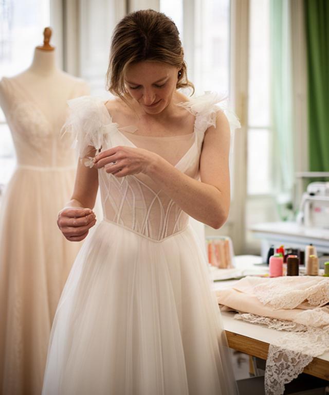 Sarta che rifinisce il corpetto di un abito da sposa in un atelier luminoso di Roma